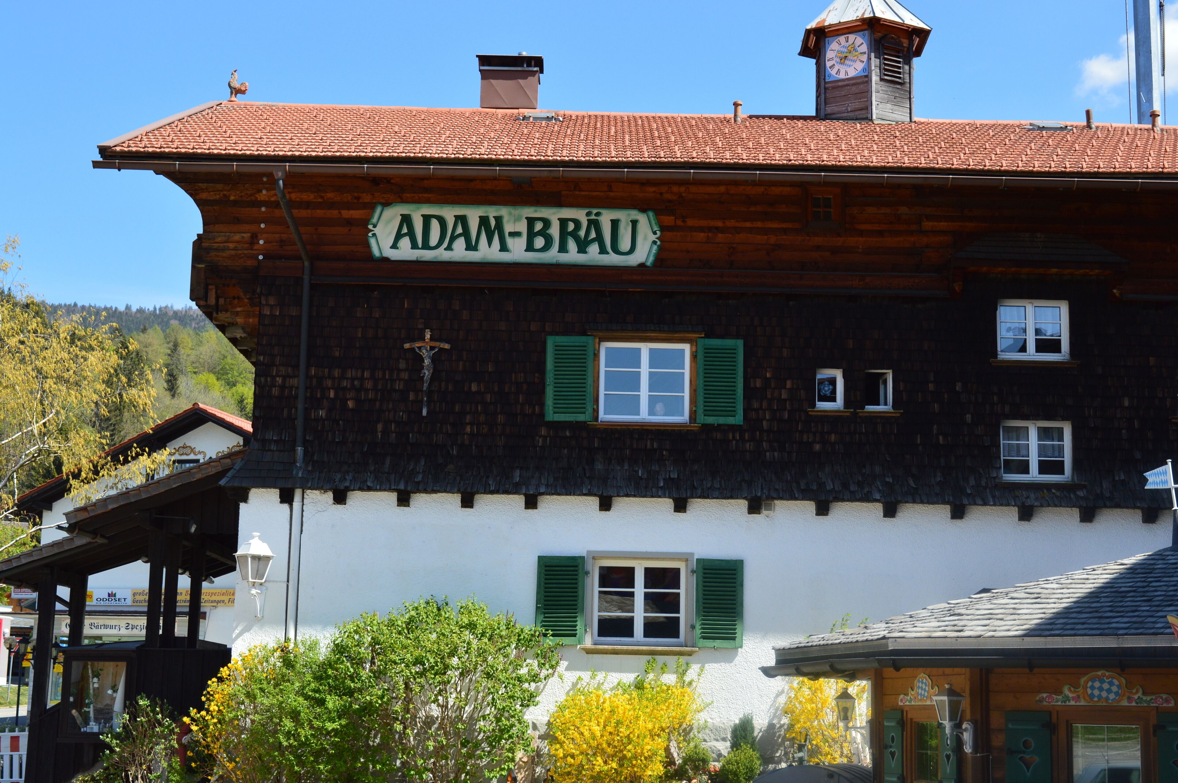 Un bâtiment traditionnel en bois, avec une enseigne portant l’inscription « ADAM-BRÄU » et des volets verts.