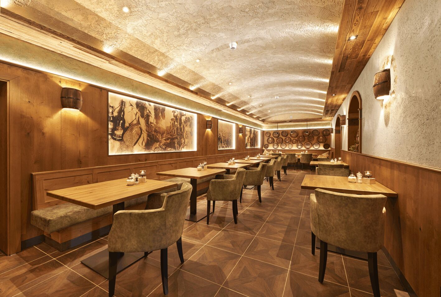 Un restaurant avec des tables et des chaises en bois, un plafond haut avec des poutres apparentes et des luminaires fixés aux murs.