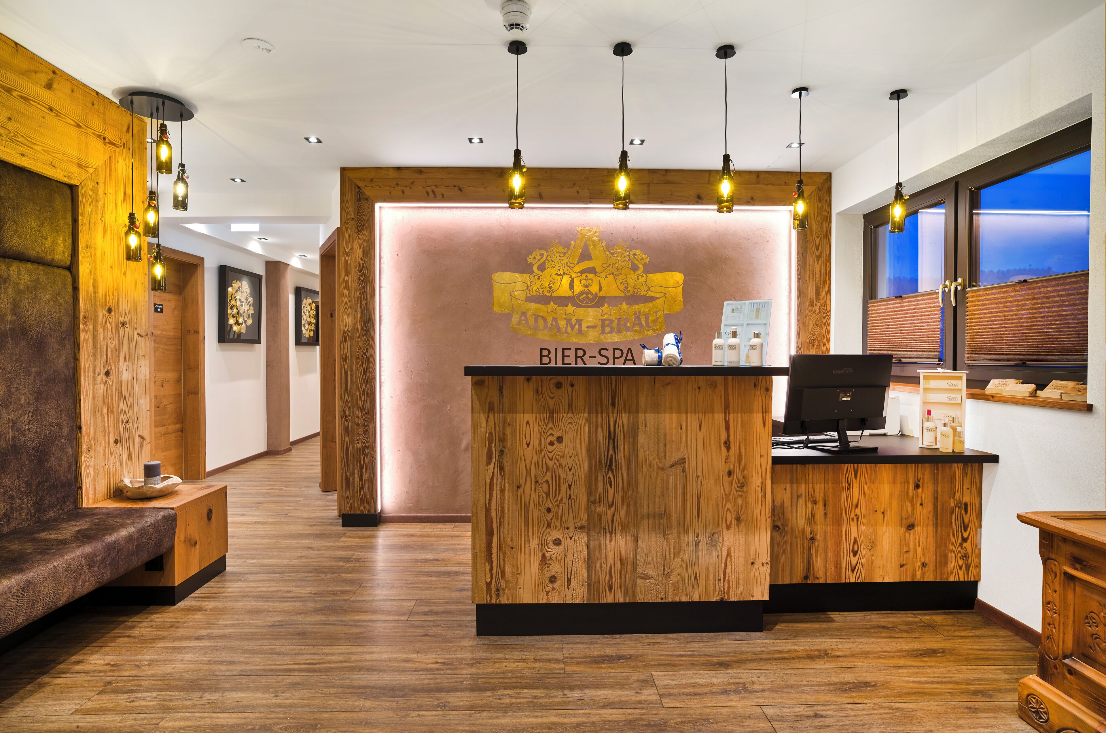 A reception desk with a wooden finish, a computer, and a counter with a sign reading "Bier-Spa".