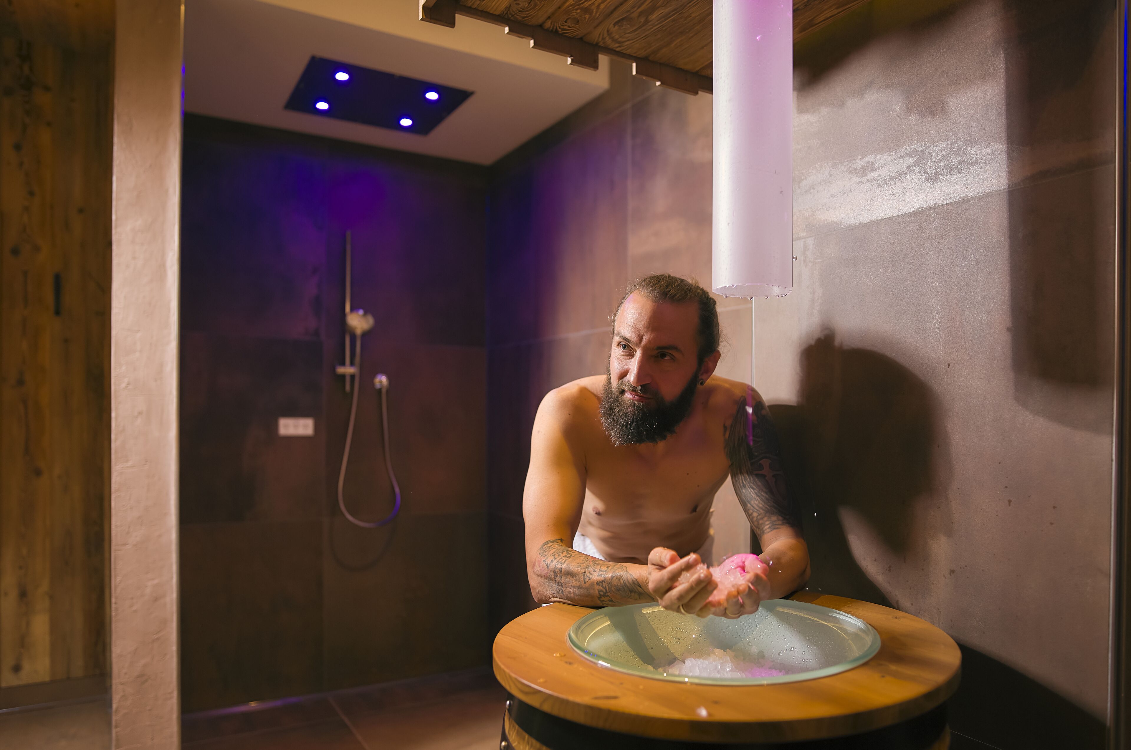 A man in a shower room with a wooden floor and a glass bowl on a wooden table.