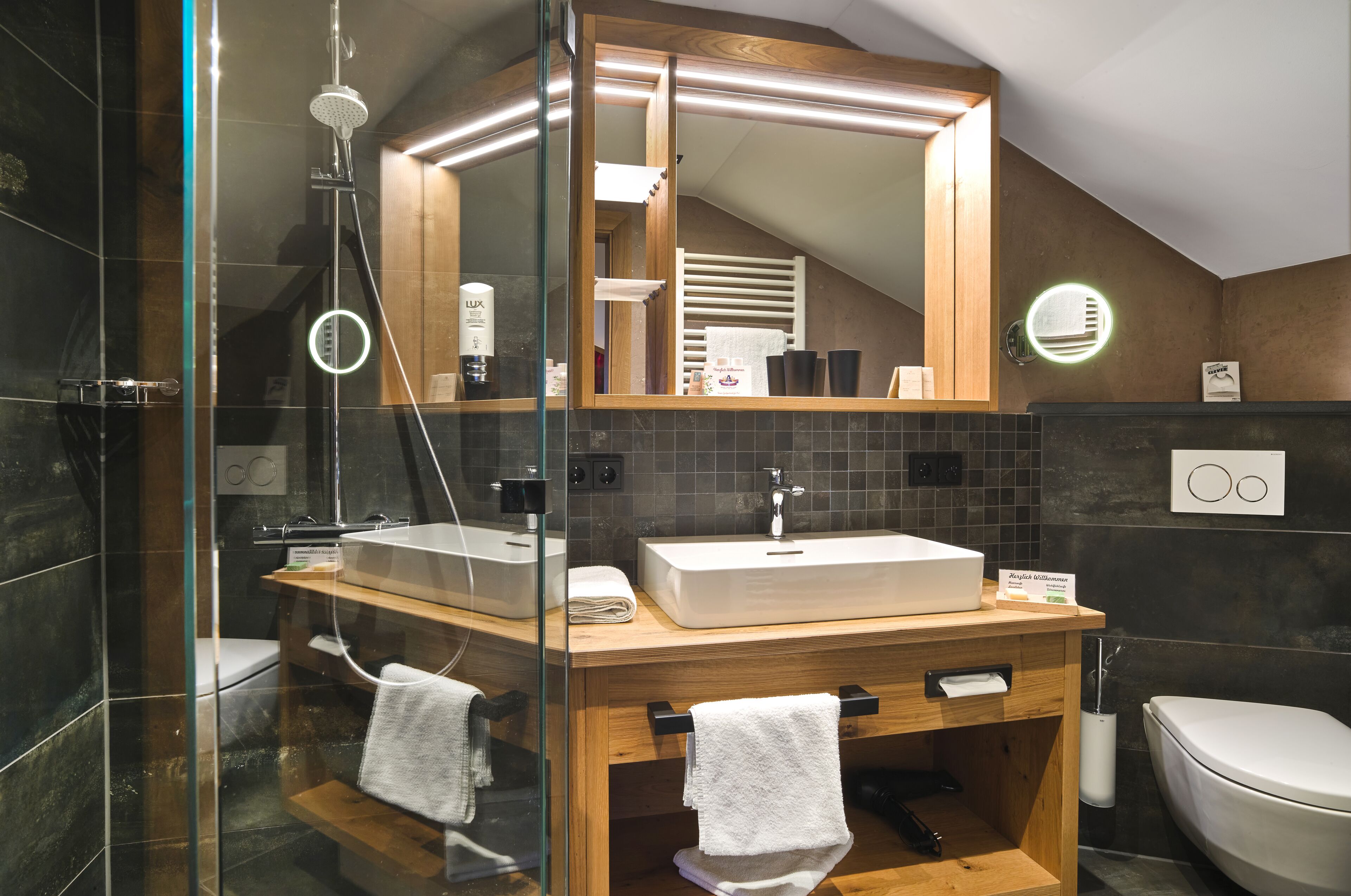 Une salle de bain moderne avec une douche à parois de verre, un meuble-lavabo en bois doté d’un grand miroir et des toilettes blanches.