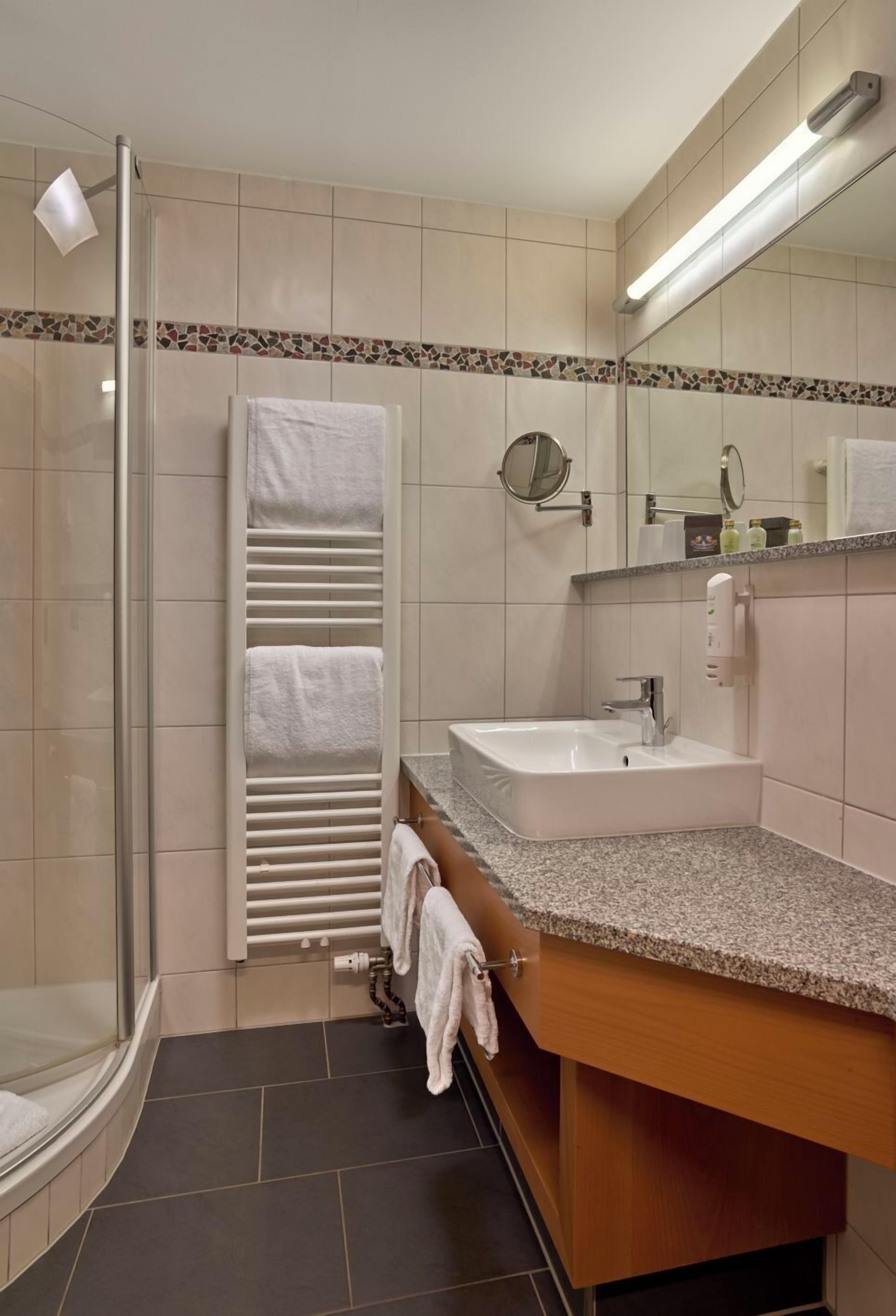 Un baño moderno con cabina de ducha de vidrio, toallero integrado, lavabo con espejo y encimera con artículos de aseo.