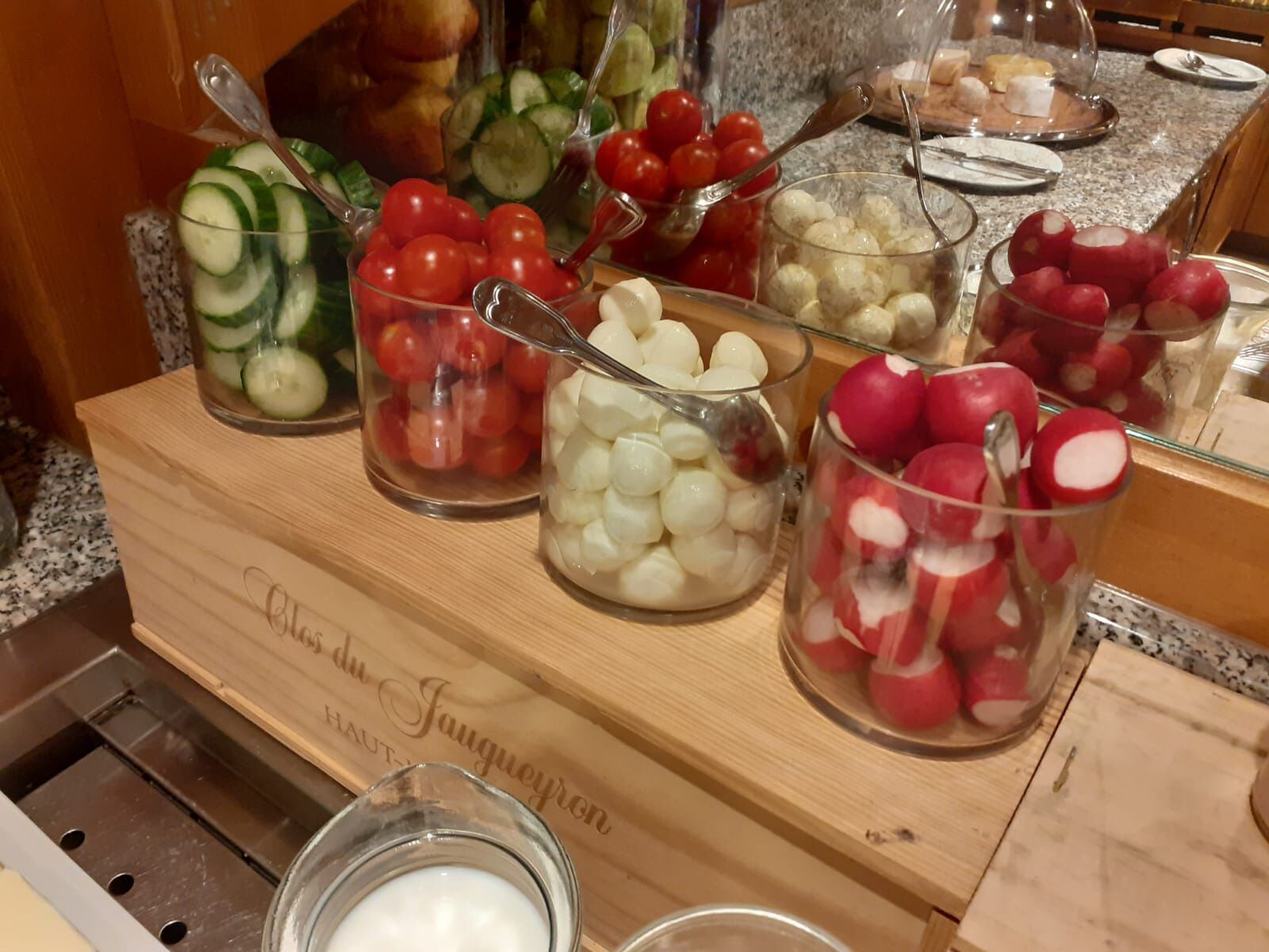 A buffet with various food items like sliced cucumbers, cherry tomatoes, and radishes in glass containers.