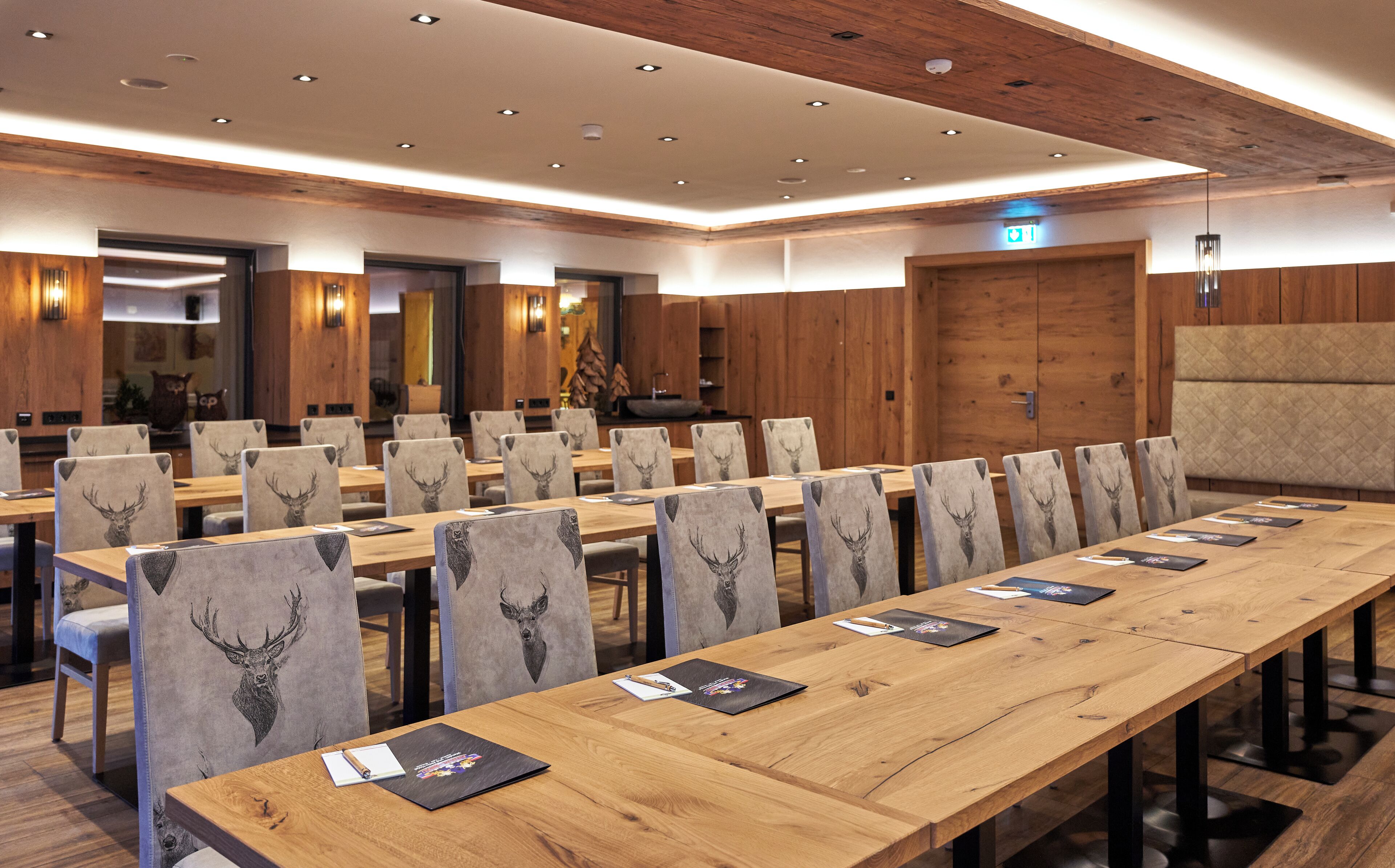Ein Konferenzraum mit langen Tischen, Stühlen mit Hirschmotiven und Holzvertäfelung.