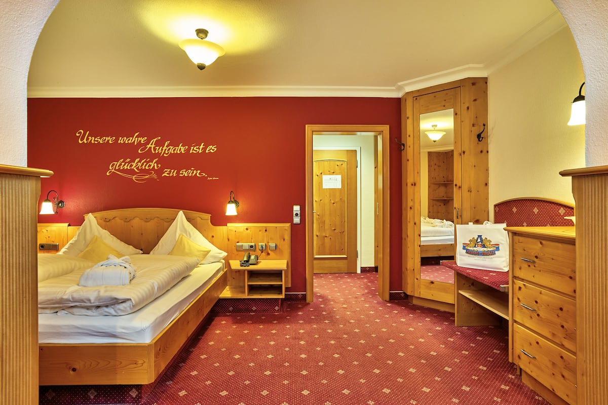 Une chambre d’hôtel avec un lit en bois, une table de chevet, une commode, un miroir et une moquette rouge.