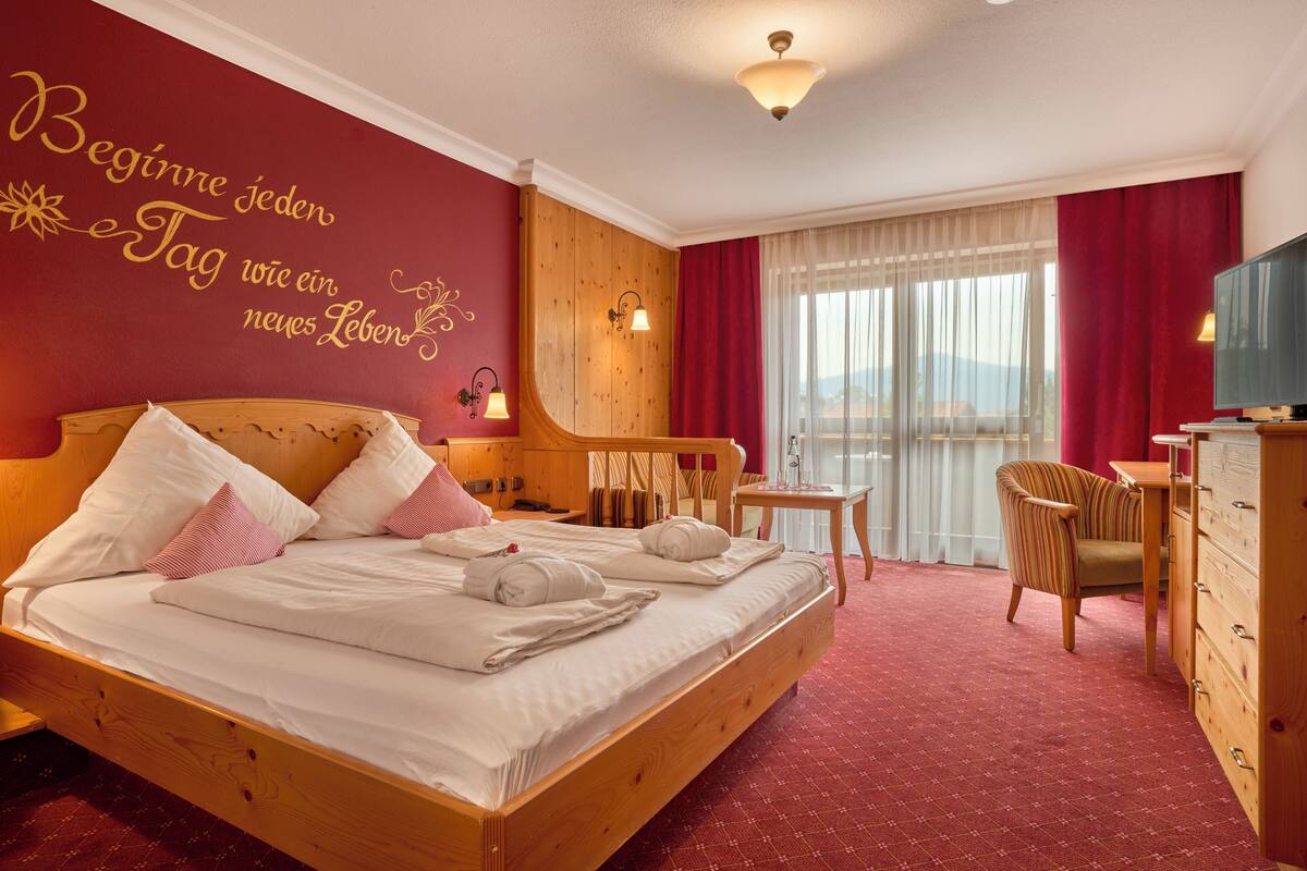 Une chambre d’hôtel avec un lit en bois, un bureau, une chaise et un téléviseur.
