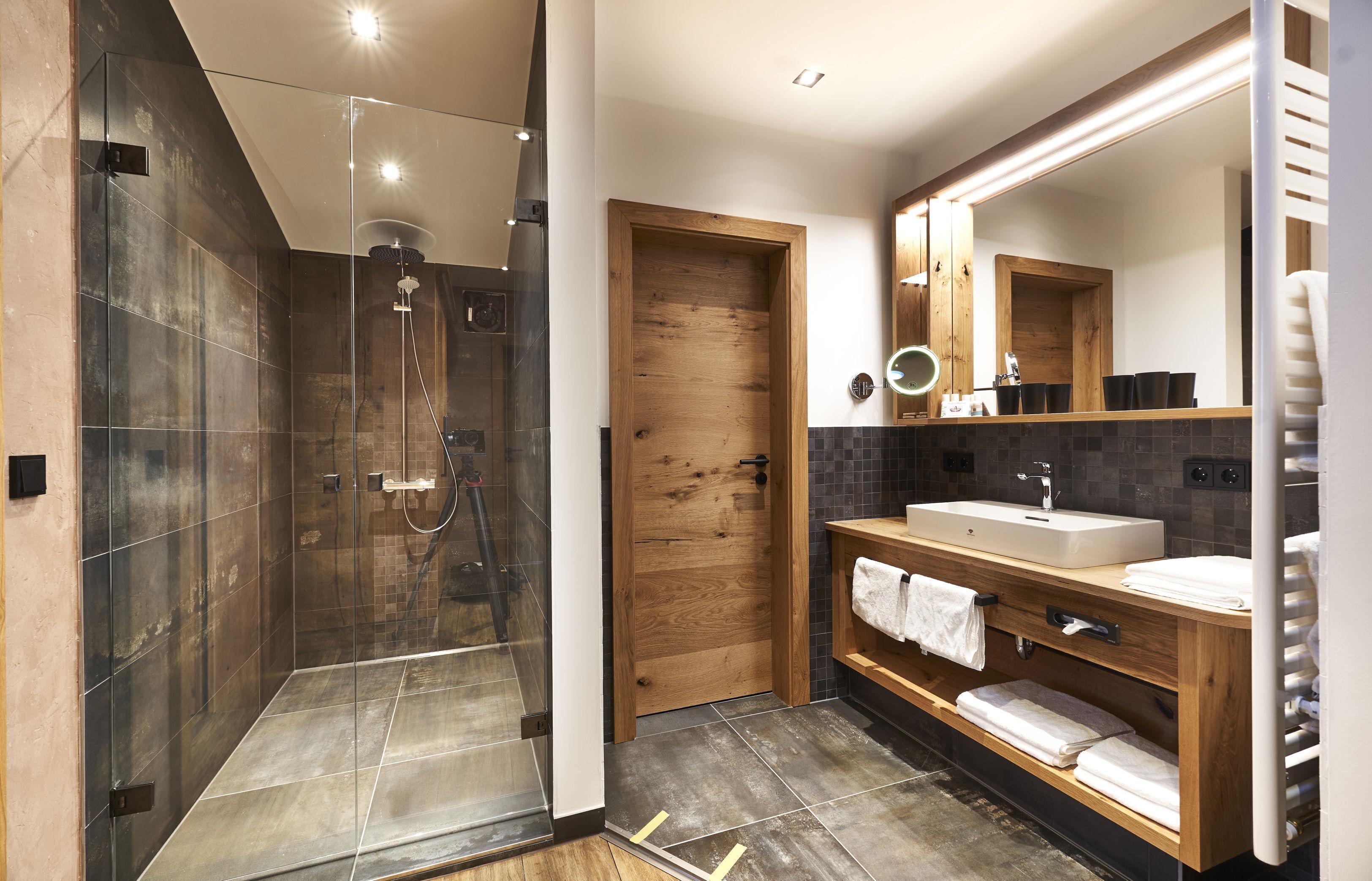 A modern bathroom with a glass-enclosed shower, a wooden door, a vanity with a sink, and a large mirror.