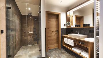 A modern bathroom with a glass-enclosed shower, a wooden door, a vanity with a sink, and a large mirror.