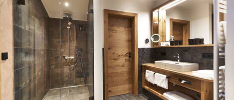 Un baño moderno con ducha de vidrio, puerta de madera, tocador con lavamanos y un espejo grande.