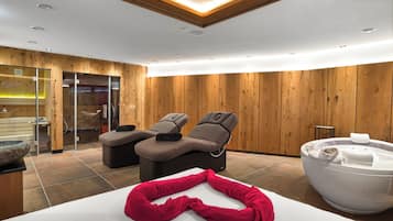Een moderne spa-ruimte met houten wanden, twee massagestoelen, een jacuzzi en een rode handdoek op de vloer.