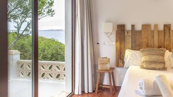 Une chambre d’hôtel avec une grande fenêtre, une tête de lit en bois, une petite table de chevet et un lit avec du linge de lit et des serviettes blancs.