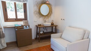 Un baño con lavamanos blanco, tocador de madera y sillón blanco.