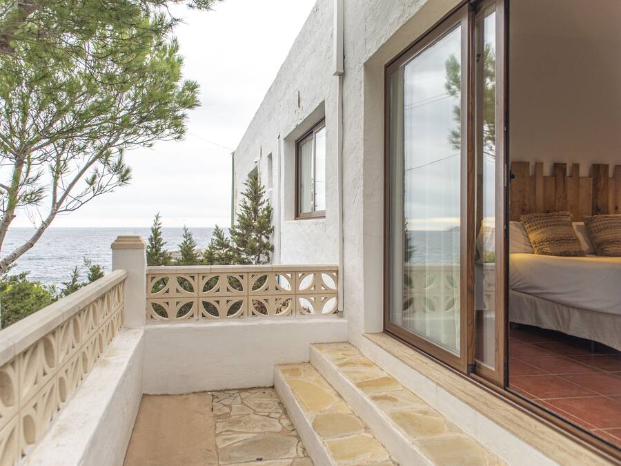 A balcony with a stone floor, a view of the sea, and a bed with pillows.
