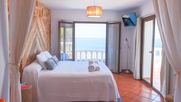 A bedroom with a bed, a TV, and a view of the sea.