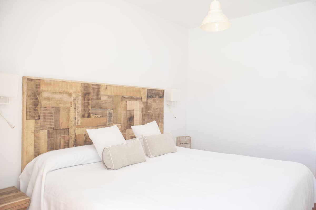 Een slaapkamer met een houten hoofdbord, twee kussens, een nachtkastje en een hanglamp.