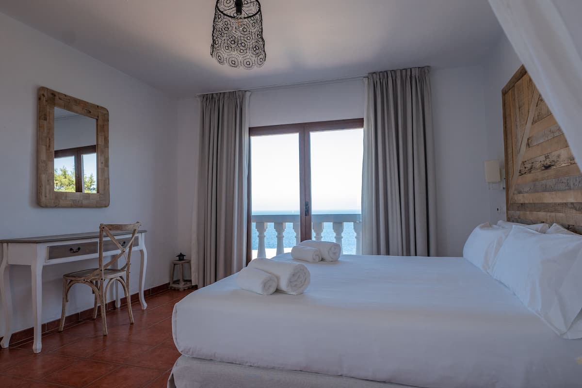 Een hotelkamer met een groot bed, een bureau, een stoel en uitzicht op zee.