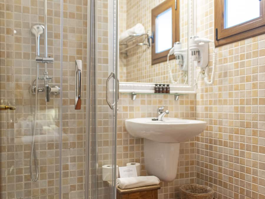 Une salle de bain avec une douche à parois de verre, un lavabo, un miroir et un petit tabouret.