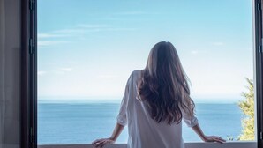 Una persona de pie junto a una ventana con vista a un cuerpo de agua.