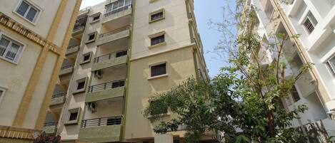 A multi-story residential building with balconies, a gated entrance, and a signboard.