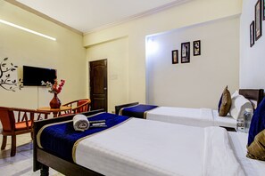 A hotel room with two beds, a desk, a chair, a TV, and a door.