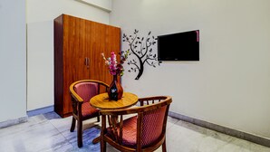 A room with a wooden wardrobe, a round wooden table with two chairs, a vase with flowers, and a wall-mounted TV.