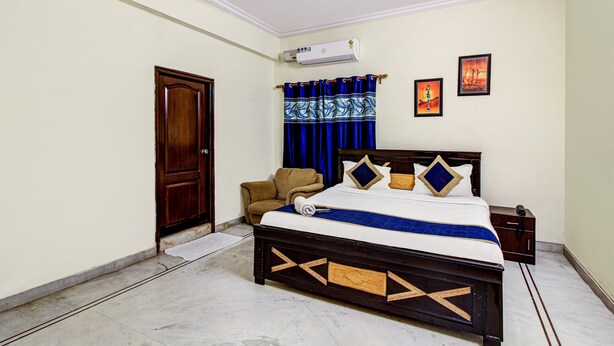 A bedroom with a bed, a chair, a wardrobe, and a wall-mounted air conditioner.