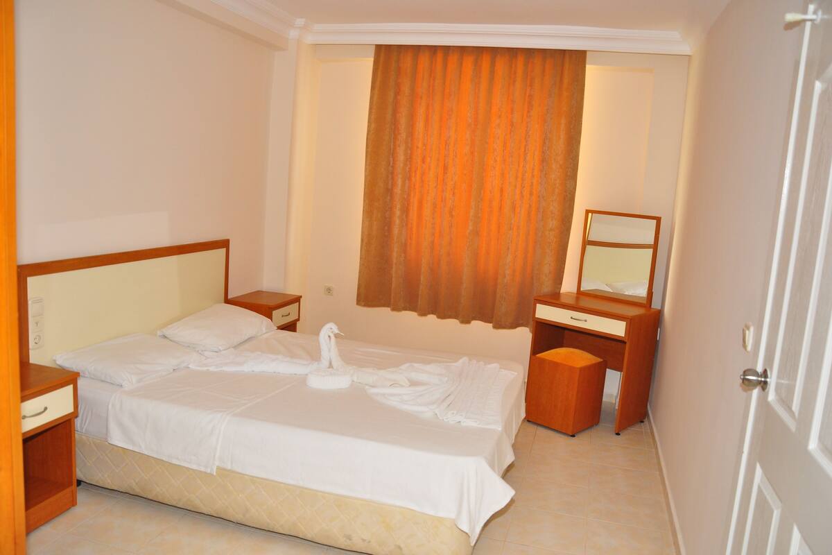 A hotel room with a bed, a bedside table, a dresser, and a mirror.