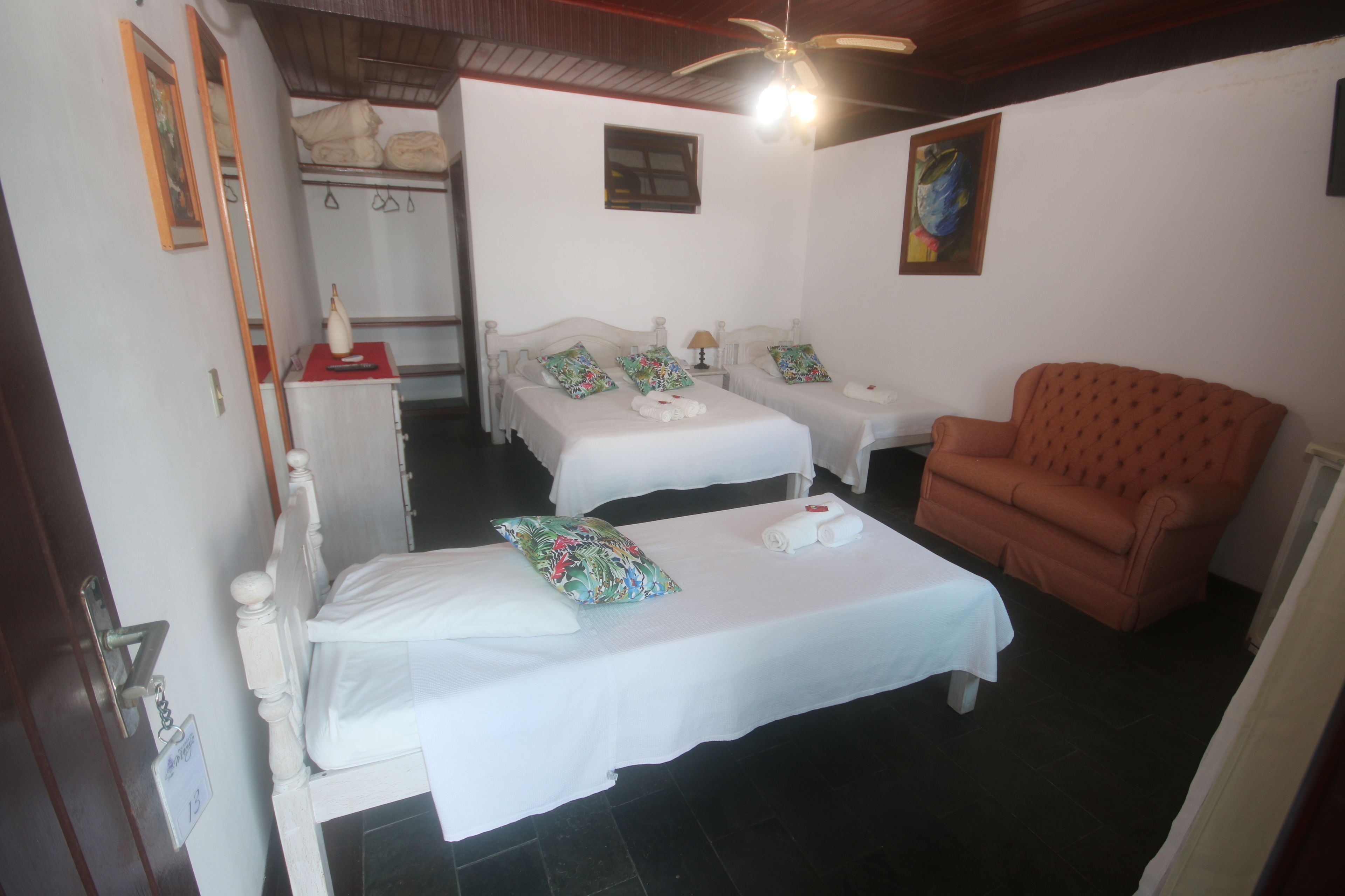 A hotel room with two single beds, a brown armchair, a small table, and a ceiling fan.
