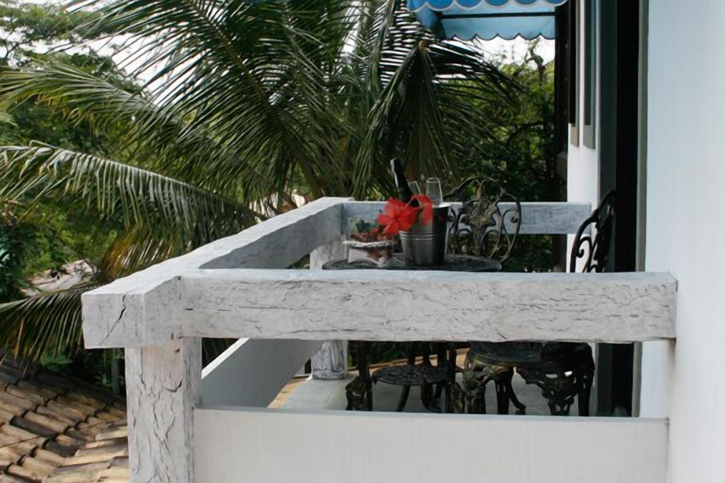 Een balkon met een stenen rand, een kleine tafel met decoratie, en uitzicht op palmbomen.