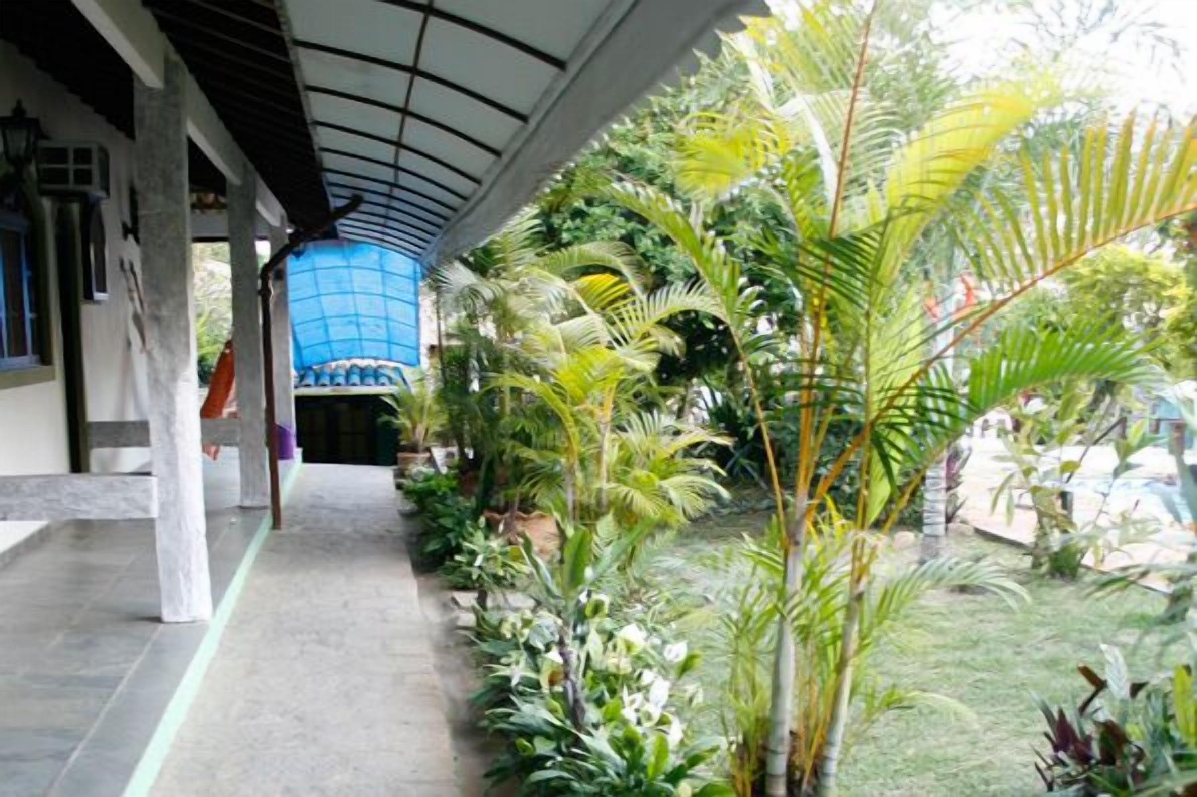 Un paseo techado con suelo de baldosas, rodeado de exuberantes plantas tropicales y una estructura de vidrio azul.