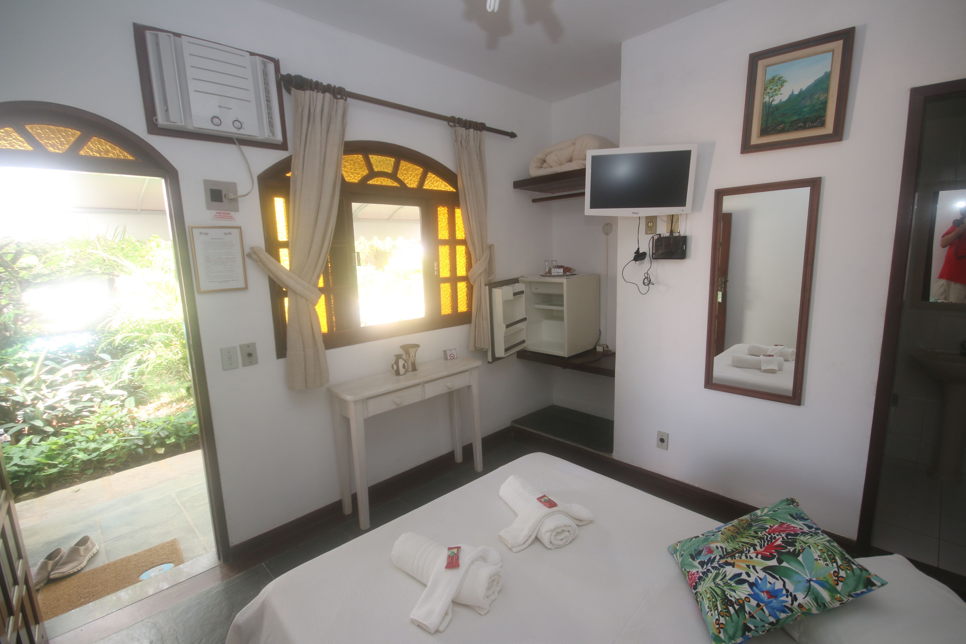 A hotel room with a bed, a desk, a TV, a mirror, and a window with curtains.