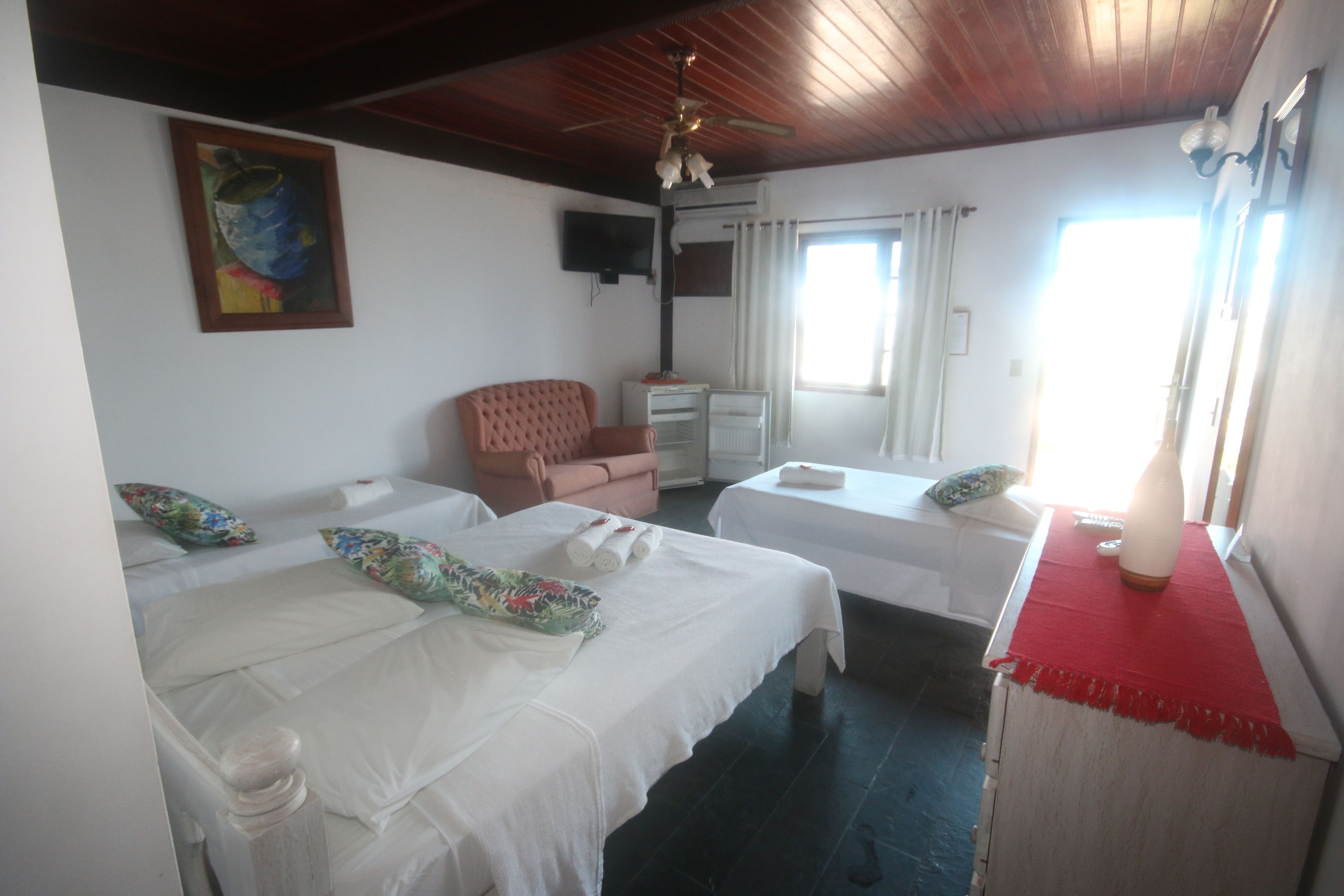 A hotel room with two beds, a television, a ceiling fan, and a window with curtains.