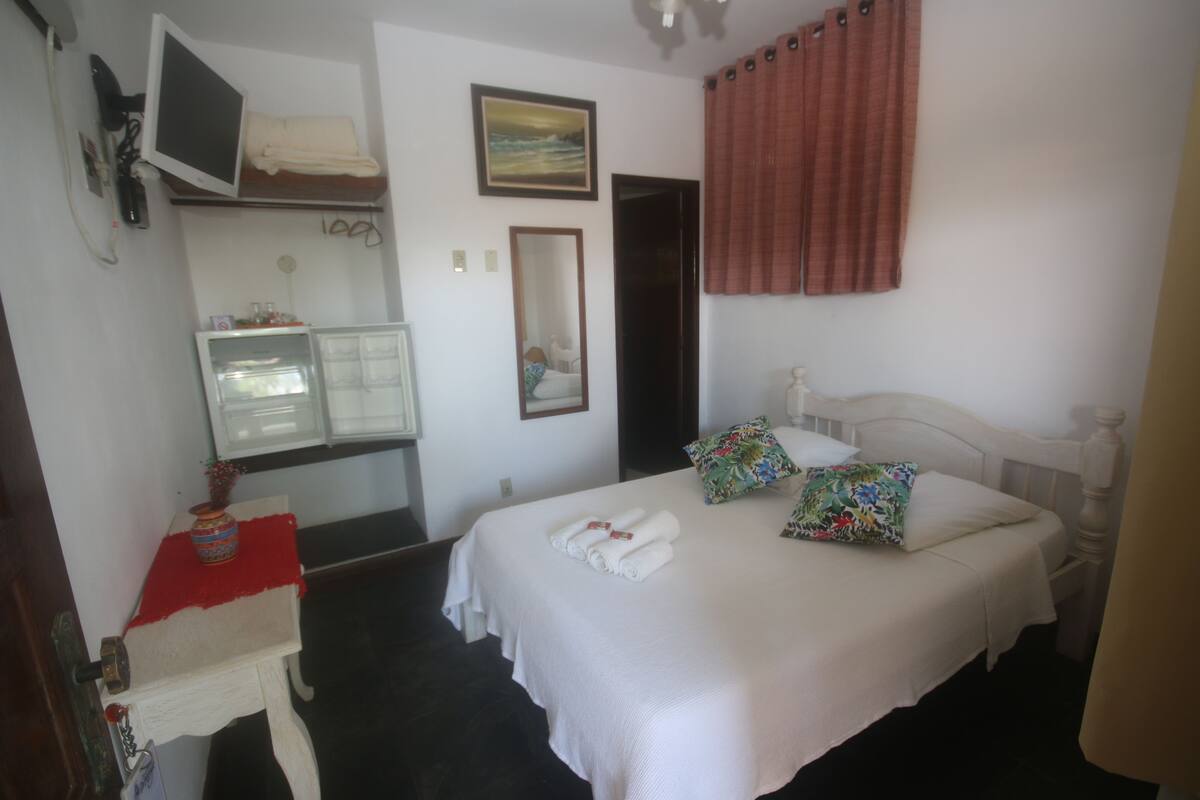 Habitación de hotel con cama, televisión sobre un mueble, espejo y ventana con cortinas.