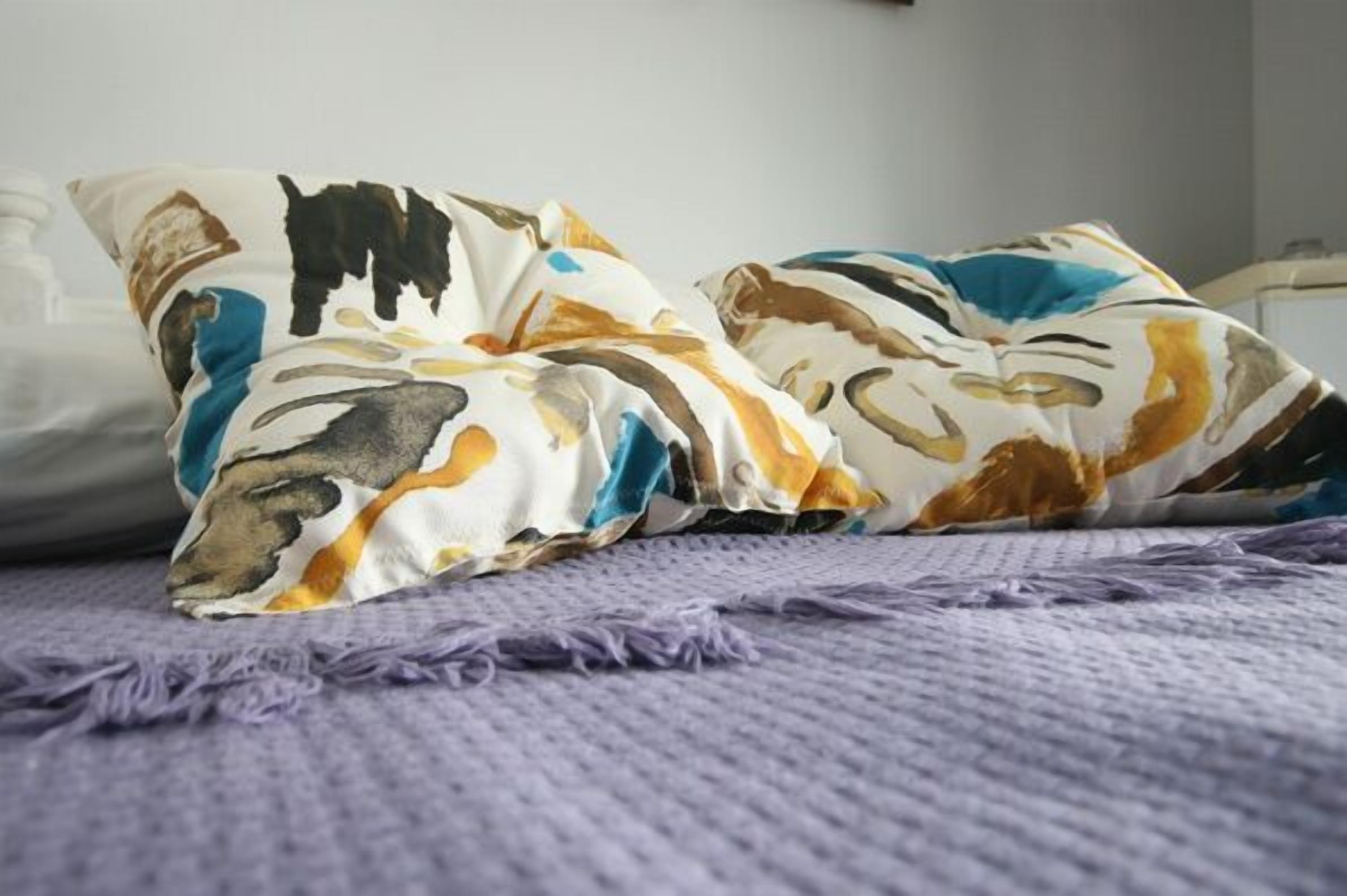 A bed with a purple blanket and two pillows with abstract patterns.