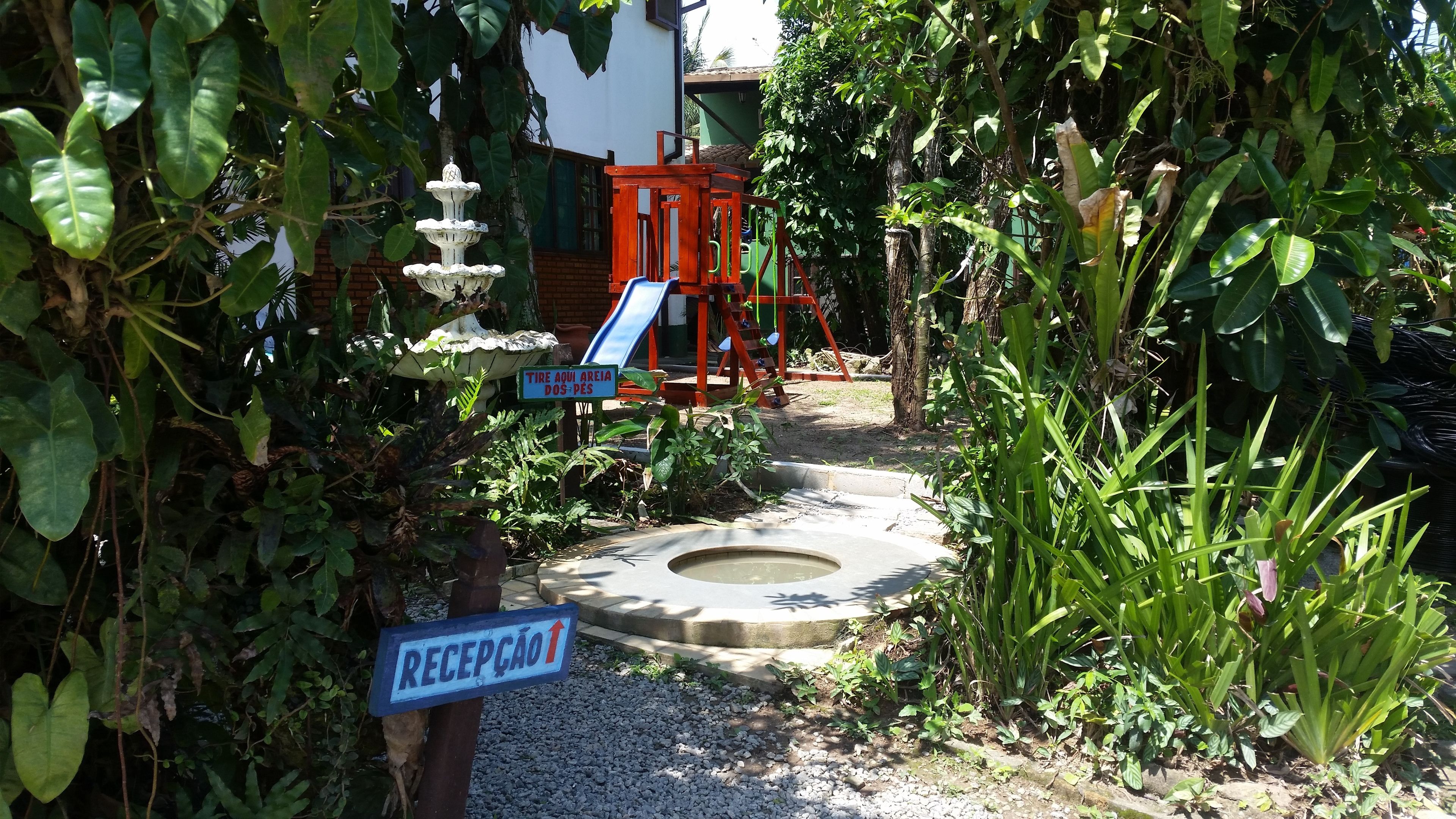 Een tuin met een kinderspeelplaats, een waterpartij en een bord met de receptie.