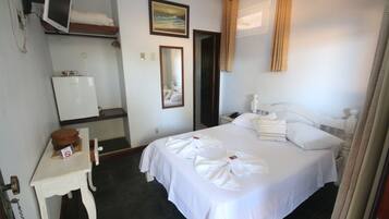 Una habitación de hotel con una cama, un escritorio con un monitor de computadora, un espejo y un cuadro en la pared.