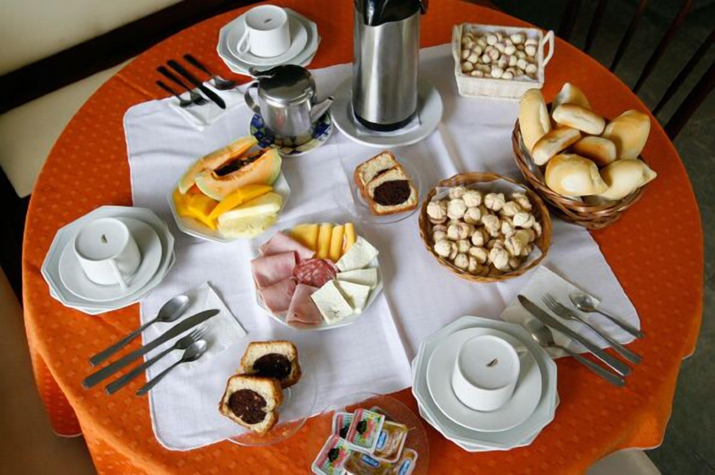 A table set with various food items, including bread, cheese, and pastries, along with cups and a coffee pot.