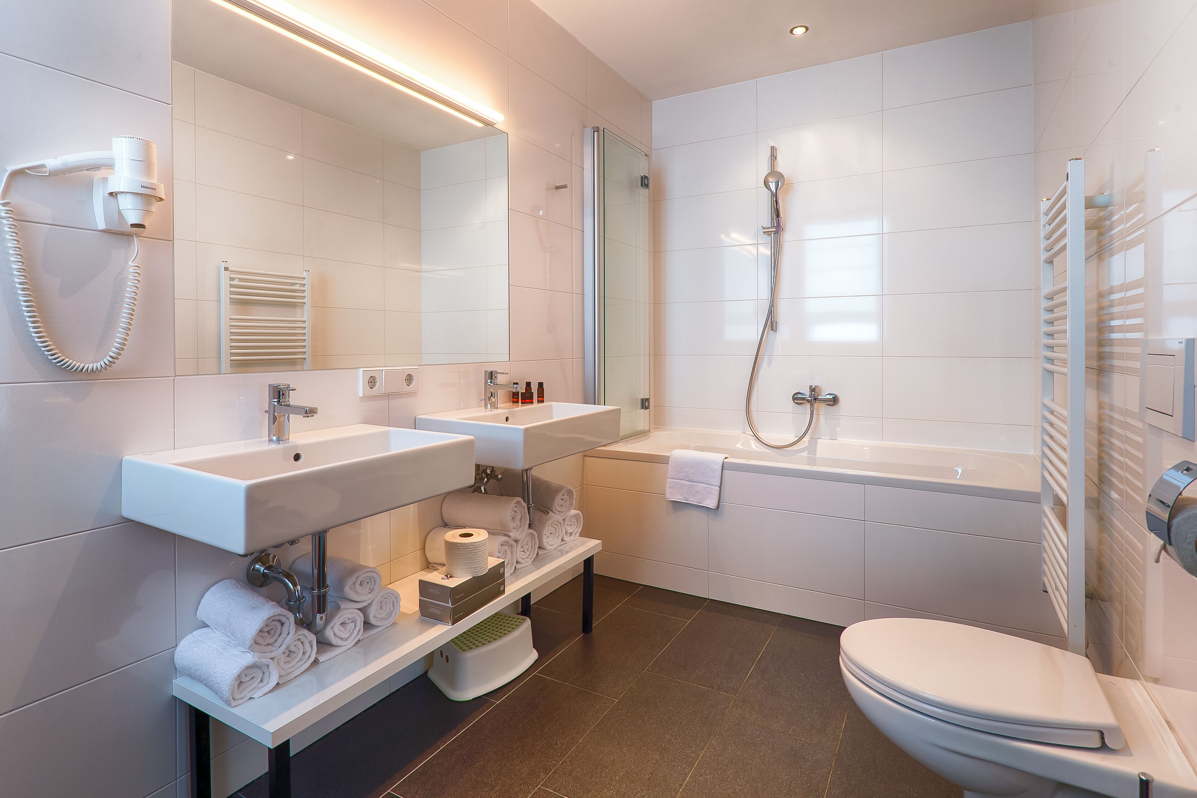 Un baño moderno con lavamanos, espejo, toallero, inodoro y ducha.