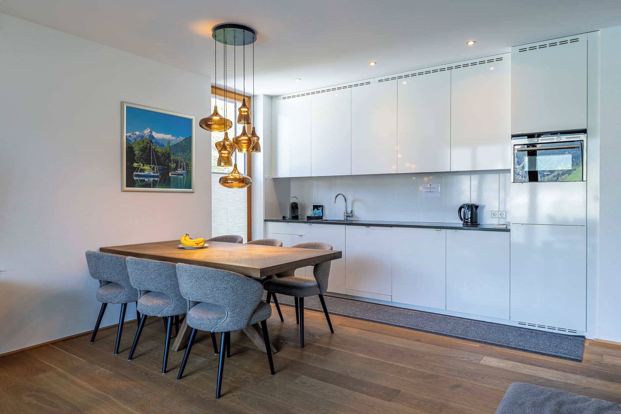 A modern kitchen with white cabinets, a wooden dining table, and grey chairs.