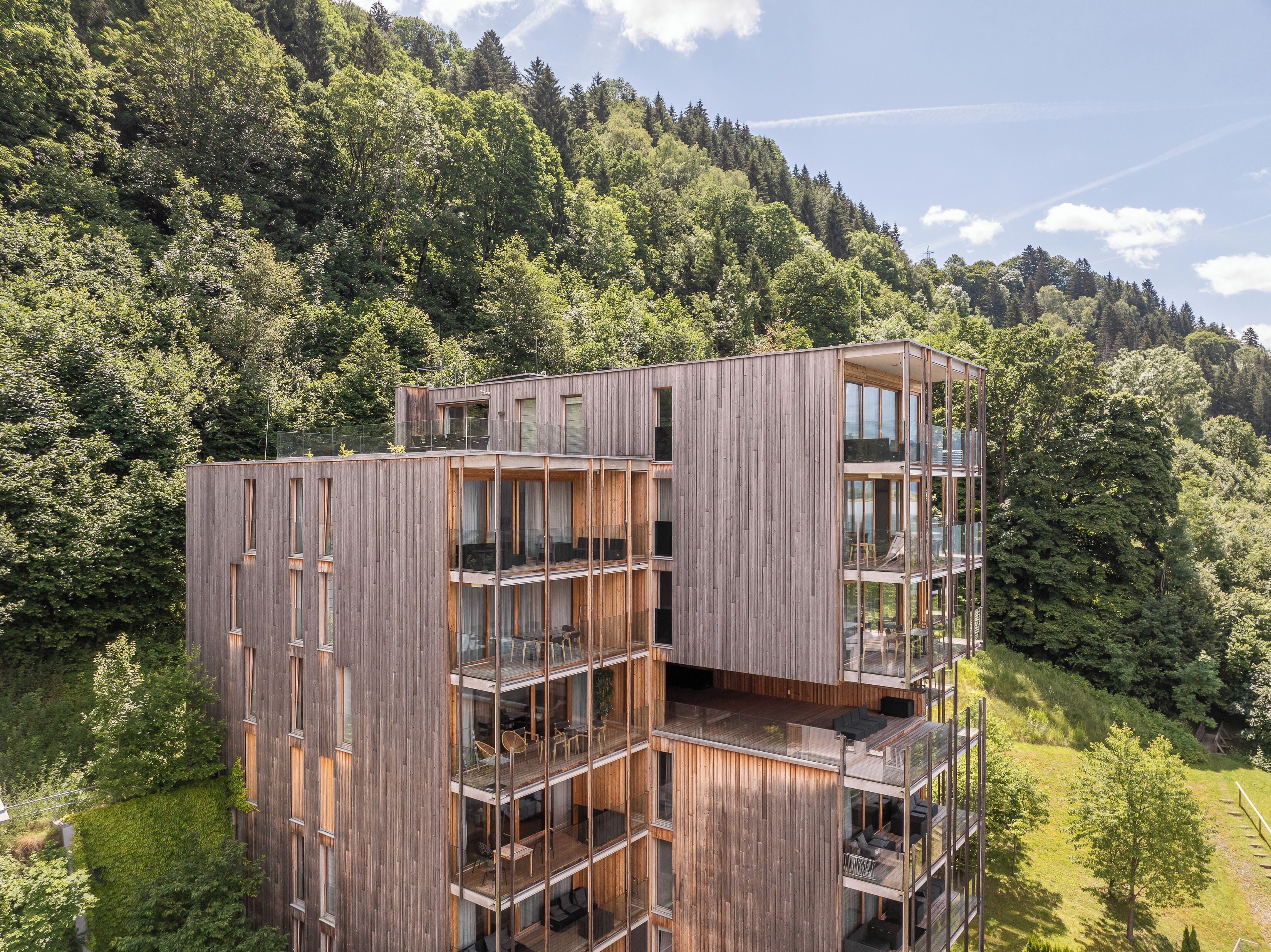 A modern multi-story building with large glass windows, wooden exterior, and balconies.
