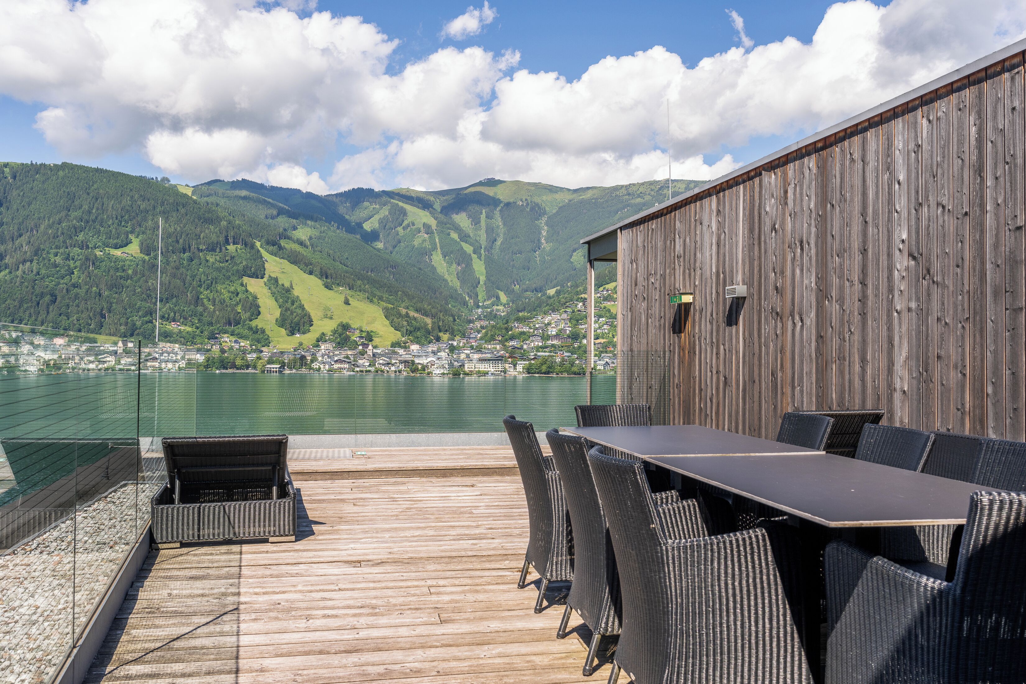 A wooden deck with a table and chairs overlooking a lake and mountains.