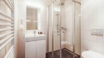 Een moderne badkamer met een douchecabine van glas, een witte wastafel met een spiegel erboven en een toilet.