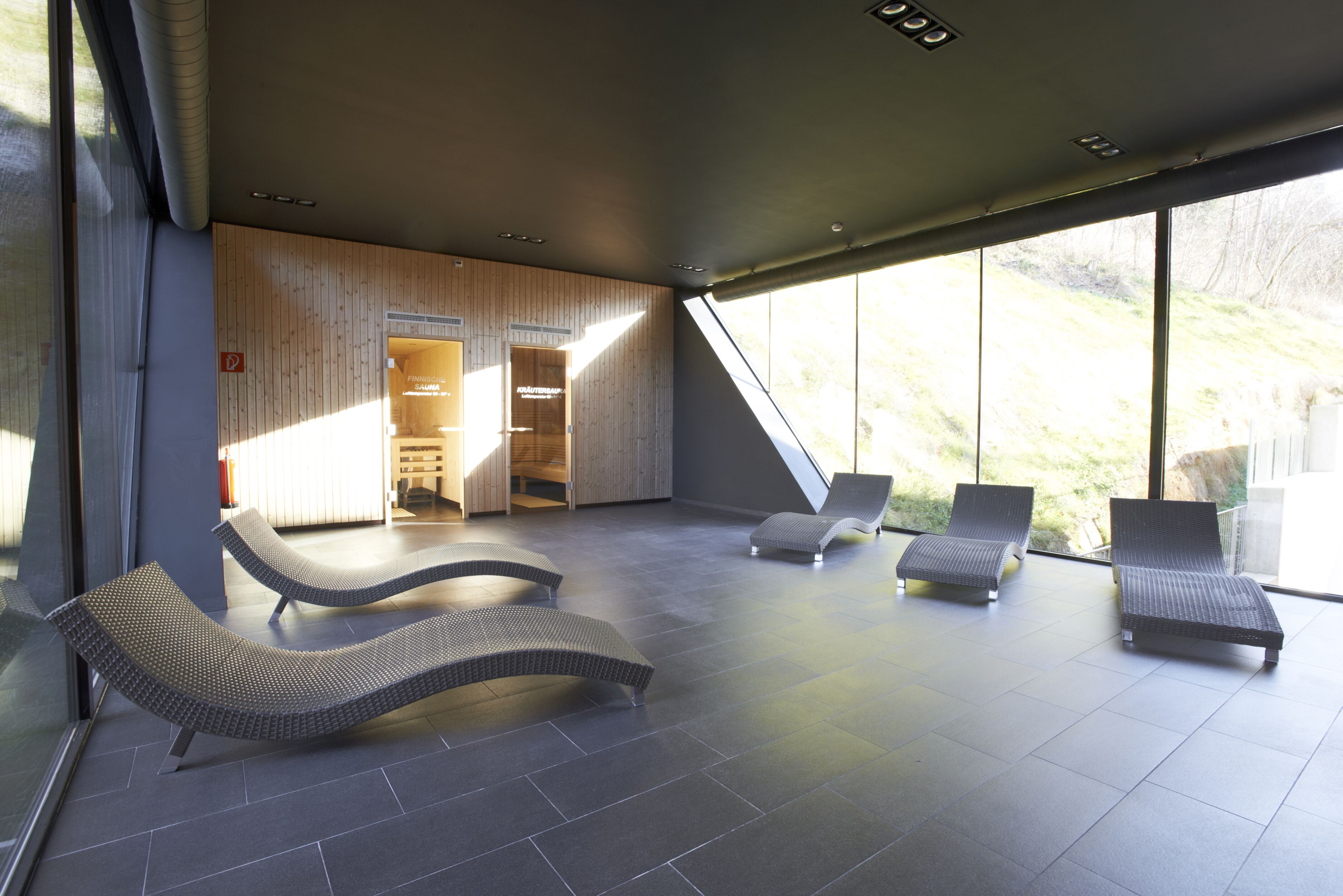 A modern spa area with three lounge chairs, a wooden wall, and large windows offering a view of the outdoors.