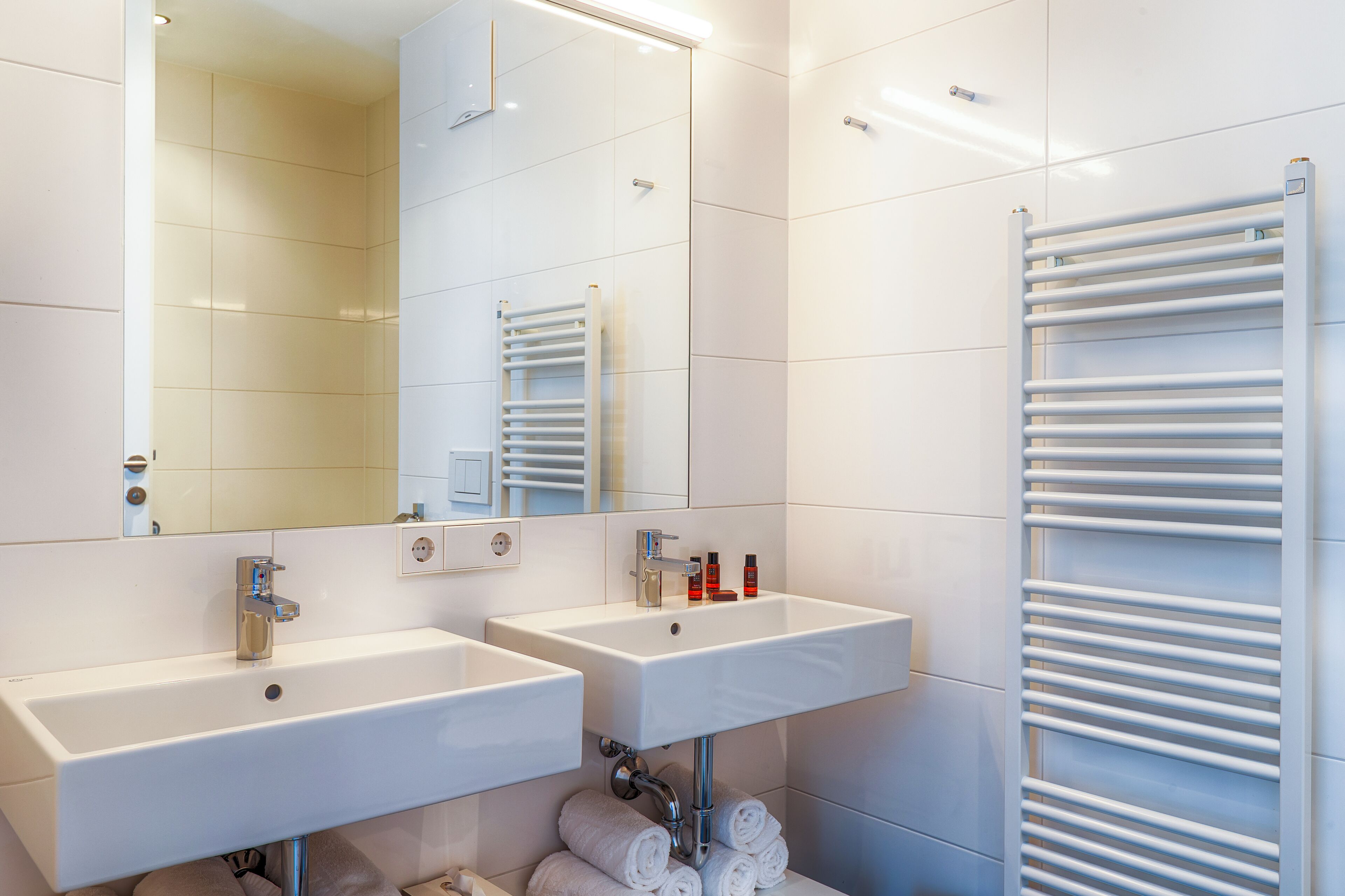 A modern bathroom with two sinks, a mirror, and a towel rack.
