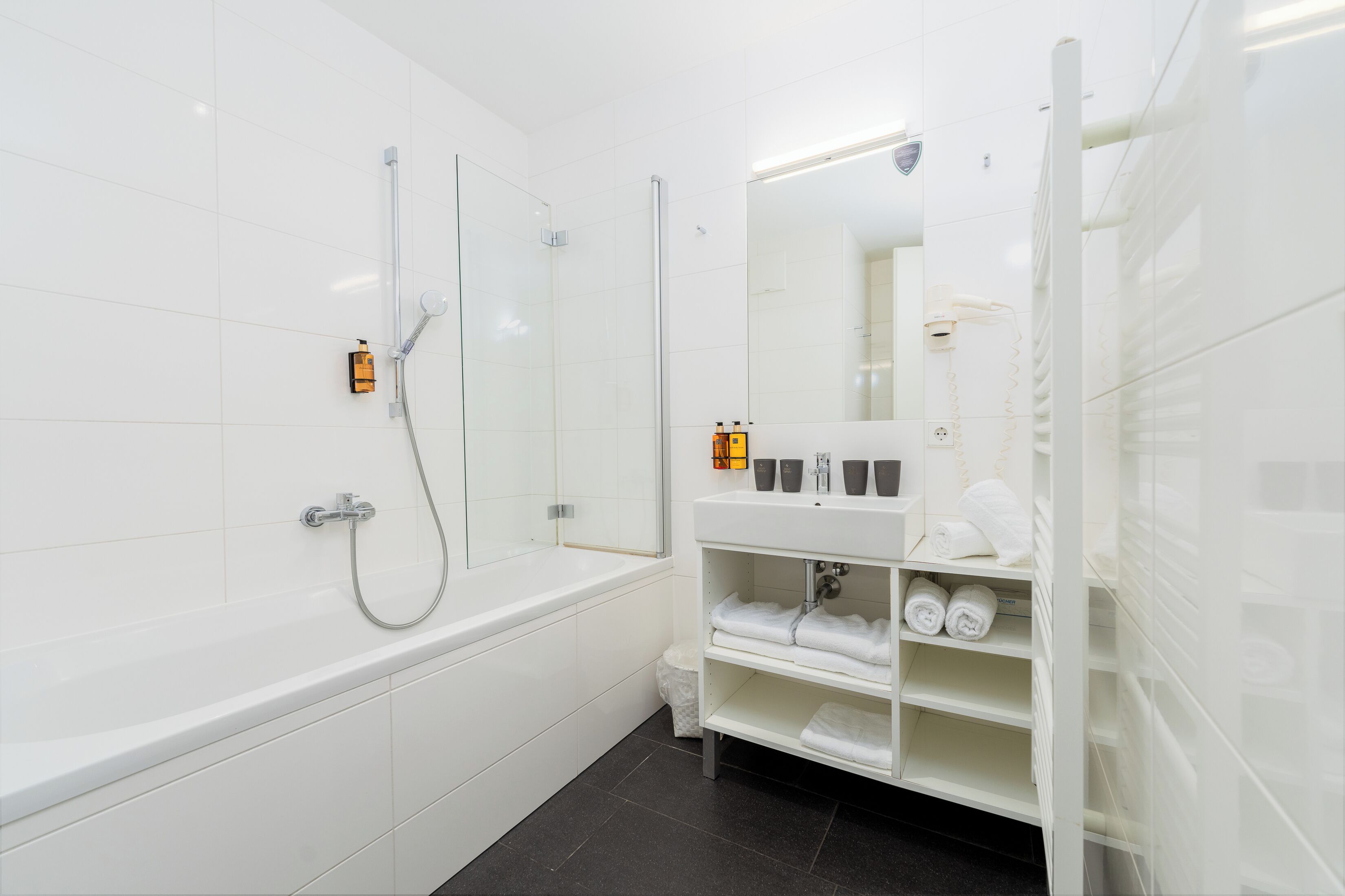 A modern bathroom with a bathtub, a glass-enclosed shower, and a vanity with towels and toiletries.