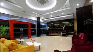 A modern lobby with a central seating area featuring yellow and red chairs, a white coffee table, and a potted plant.