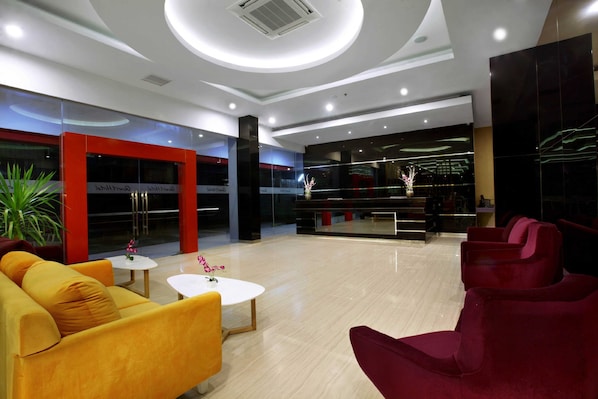 Un vestíbulo moderno con una zona de estar central, sillones amarillos y rojos, una mesa de centro blanca y una planta en maceta.