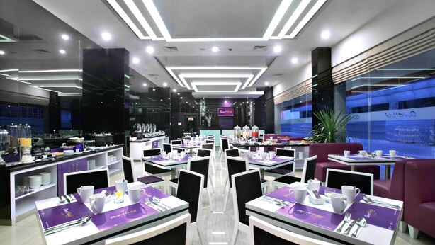 A modern hotel restaurant with a central dining area, multiple tables, and purple placemats.