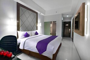 Habitación de hotel con una cama grande, una silla y una mesa con manzanas.