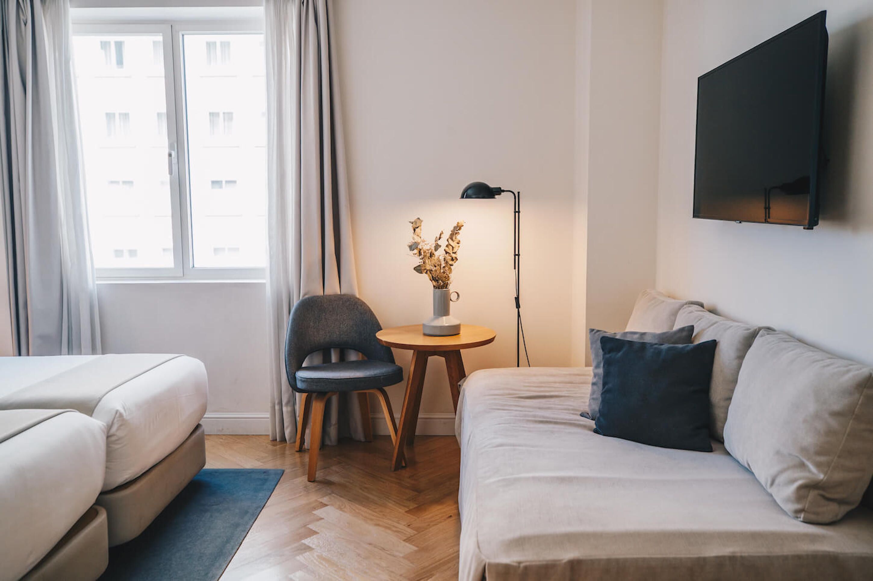 Una habitación de hotel con una cama, un sofá, una silla, una mesita de noche con una lámpara y un televisor en la pared.